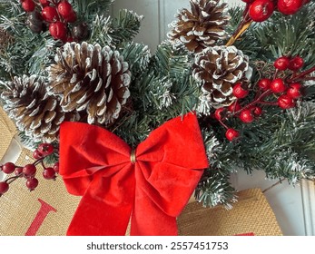 Close-up of a festive Christmas wreath featuring frosted pinecones, vibrant red berries, and a bold red bow, capturing the warmth and charm of holiday decorations on a door. - Powered by Shutterstock