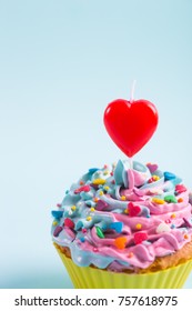 Closeup Festive Creamy Cupcake With Sprinkles And Candle In Form Of Red Heart On Purple Background. Romantic Cake For St. Valentine's Day