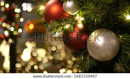 Closeup of Festively Decorated Outdoor Christmas tree with bright red balls on blurred sparkling fairy background. Defocused garland lights, Bokeh effect. Defocused night city street, cars on road.