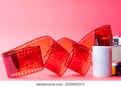 A close-up of a film reel with a strip of red film unwinding against a pink background. The film strip features perforations along the edges, showcasing a classic design - Powered by Shutterstock