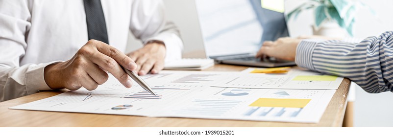 A Close-up Of A Financial Businessman Holding A Pen And Pointing At The Information Sheet On His Desk, Reading The Company's Financials To Make A Financial Plan. Financial Concept.