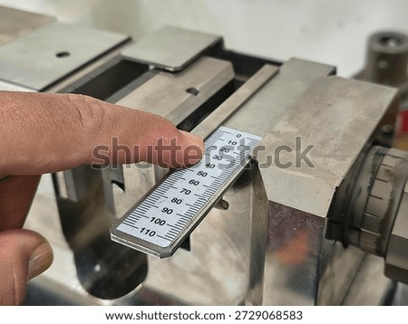 Close-up of a finger pointing at a measuring scale on an industrial testing machine, precision calibration and material strength analysis in a professional laboratory setting