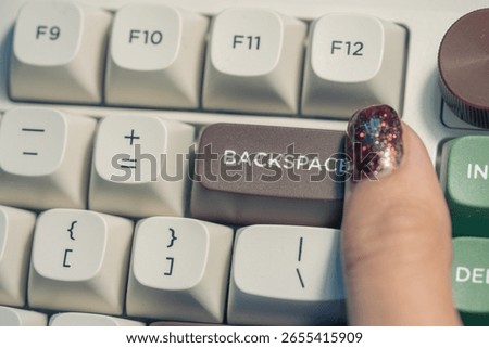 Close-up of a finger pressing the backspace key on a colorful mechanical keyboard with glitter nail polish.

