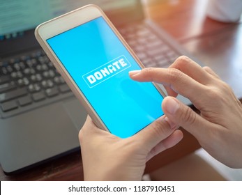 Gros plan sur le doigt en appuyant sur le bouton d'icône de don sur l'écran bleu sur un téléphone portable blanc avec ordinateur portable noir sur une table en bois. Concept de don en ligne.