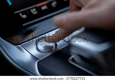 Close-up of finger pressing engine start stop button in modern car, showing ignition control on center console inside vehicle.