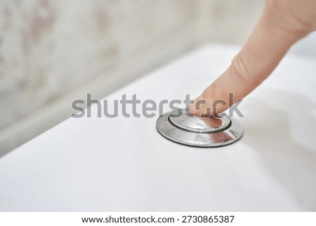 Close-up of finger pressing silver button on white flush toilet for bathroom hygiene concept.