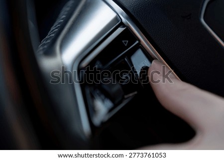 Close-up of finger pressing view button on steering wheel in modern car, showing multifunction control area for instrument cluster and display settings.