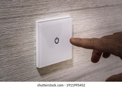 A close-up finger turns on the light on the touch switch. A white modern light switch on a white wall. modern design. turn-on turn-off - Shutterstock ID 1911995452