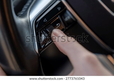 Close-up of finger using steering wheel control buttons and scroll wheel in modern car, showing multifunction interface for driver settings.