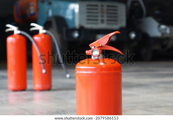 A close-up of a fire extinguisher against the backdrop\
of two other fire extinguishers and a large car.                   \
            
