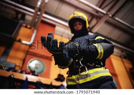 Closeup of fireman putting on gloves and preparing for action while standing in fire station.
