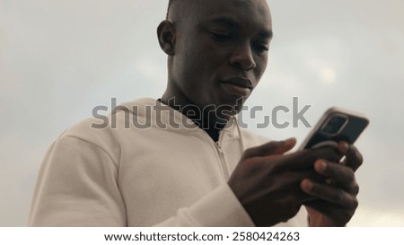 Close-up of a fit guy smiling while using mobile phone and chating outdoors, scrolling social networks