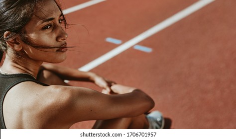 Close-up of a fit woman after run sitting on race track. Determined female athlete sitting on the field and looking away. - Powered by Shutterstock