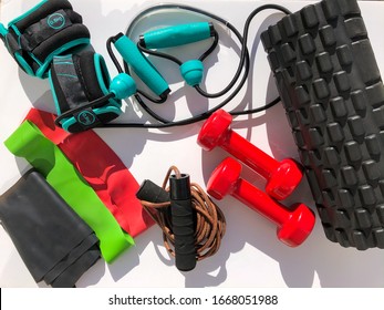 A Closeup Of A Fitness Class Equipment On A White Background Containing Elastic Strips, Foam Roller, Jump Rope, Weights, Dumbbell, Resistance Bands With Holders. Home Gym Equipment.