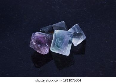 Close-up of five octahedral translucent raw fluorite mineral stone. Specimen of natural minerals - fluorite crystal on dark polished slab. Selective focus.