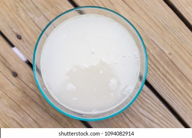 Closeup Flat Top Lay View Down Of Soaked Rice, Grain, Cloudy Liquid Water In Glass Bowl On Wooden Background