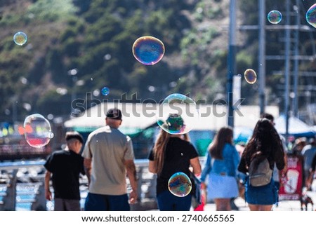 Close-up of a floating soap bubble against a bright coastal background with blurred people walking along the promenade. Sunny seaside atmosphere in San Antonio, Chile.