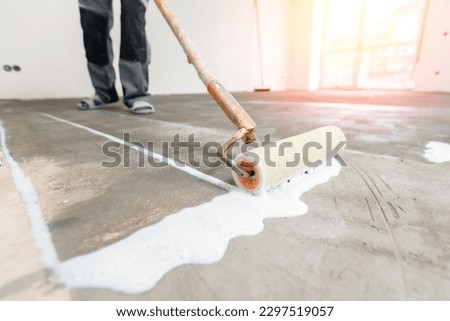 Closeup floor priming process with sun light. Worker use primer on concrete floor before leveling, strengthening surface.