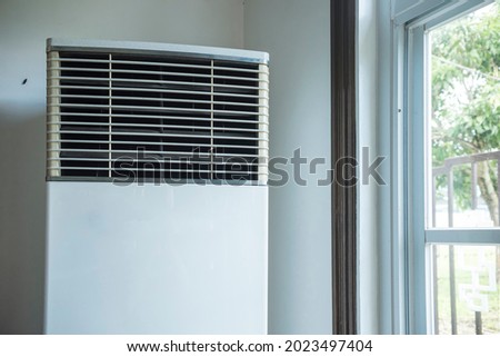 Closeup of a floor standing air conditioner or a Tower AC by the window of a restaurant or lobby.