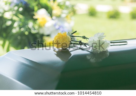 A closeup of flowers atop a funeral casket outdoors.