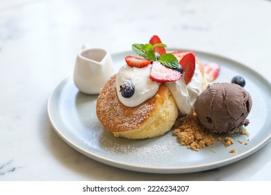 Close-up fluffy Japanese soufflé pancakes with mixed berries and chocolate ice cream dessert served with honey sauce.
