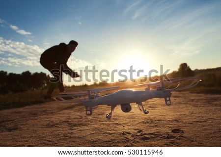 Close-up of flying drone at sunset, free space on sky background. Silhouette of young man, piloting quadrocopter outdoor. Leisure, entertainment, innovation, modern technologies concept