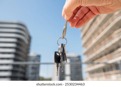 Close-up focus on house key in female hand, against new apartments, cityscape in background. Concept of new home, real estate, and success. - Powered by Shutterstock