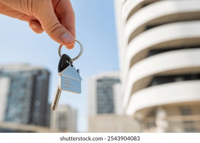 Close-up focus on house key in female hand, against new apartments, cityscape in background. Concept of new home, real estate, and success. - Powered by Shutterstock