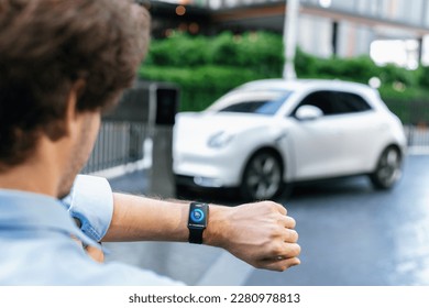 Closeup focus progressive wearable watch show electric car battery status that being recharge at charging station point in the city. Digital interface, data from EV car display on smartwatch. - Powered by Shutterstock