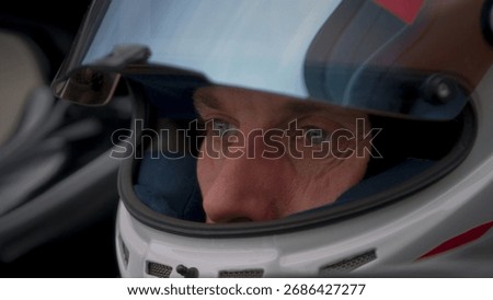 Close-up of a focused pilot driver in a red racing car, wearing a helmet, preparing for a high-speed race