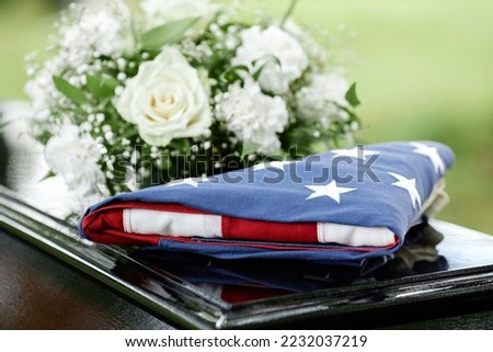 Closeup of folded American flag on coffin with flowers at outdoor funeral ceremony, copy space