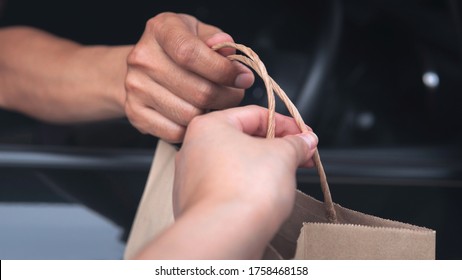 Closeup Food Delivery Man Driver’s Hand Pass Pick Up Environmentally Friendly Craft Brown Paper Bag To Customer Out Of Car Window Meeting Social Distancing Requirements And Supporting Small Businesses