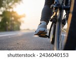 Closeup foot of the bicycle rider on the pedal while riding along the asphalt road in countryside at sunset