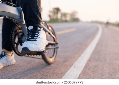 Closeup foot of a woman wearing white sneakers stepping on the pedal, going to start riding a bicycle on the asphalt road in countryside - Powered by Shutterstock