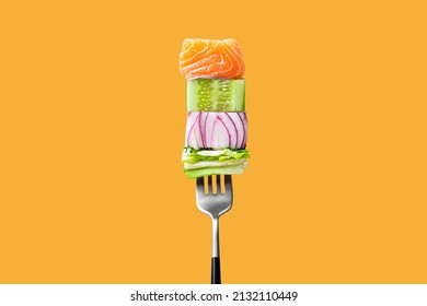 Close-up of fork with food on it: delicious fillet salmon, cucumber, onion, green salad on orange background. Concept of healthy diet and clean eating with fish and vegetables, balanced nutrition