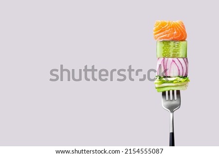 Close-up of fork with food on it: delicious fillet salmon, cucumber, onion, green salad on gray background. Concept of healthy diet and clean eating, balanced nutrition space for text