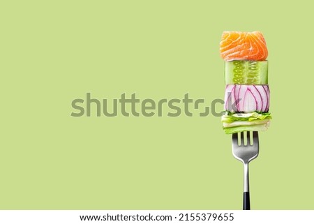 Close-up of fork with food on it: delicious fillet salmon, cucumber, onion, green salad on green background. Concept of healthy diet and clean eating, balanced nutrition space for text