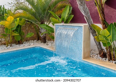 Close-up of a fountain waterfall in a luxury pool near the hotel with palm trees for tourists.