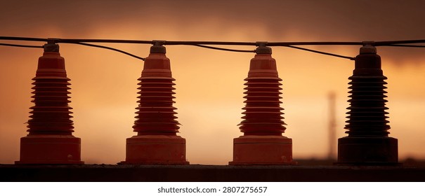 Close-up of four electrical insulators mounted on a wire, silhouetted against a warm, orange sunset sky.