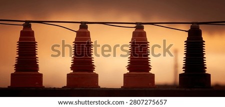 Close-up of four electrical insulators mounted on a wire, silhouetted against a warm, orange sunset sky.