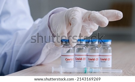 Close-up four glass bottles with covid19 vaccine against coronavirus pandemic stand on wooden table in hospital clinic laboratory near syringe hand in latex gloves takes one dose pharmacist medicine