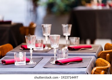 Closeup Of Four Glasses On Empty Restaurant Table In Italy, Italian Cafe Outside With Red And Blue Purple Pink Colors And Nobody