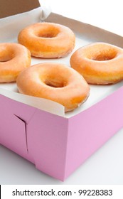 Closeup of four glazed donuts in a pink bakery box. Vertical format with a white background.