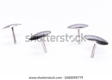 Close-up of four silver upholstery tacks against a white background. The shiny metal fasteners are arranged to show their shape and details.