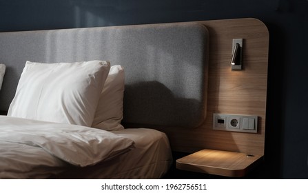 Close-up fragment of bedroom with empty bedside table, reading lamp and a USB socket in modern interior​ design home or hotel. Soft pillow and blanket, stylish comfortable furniture. Sun shadows. - Shutterstock ID 1962756511