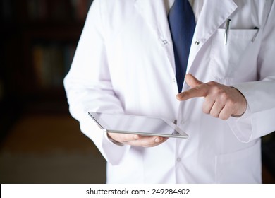 Close-up fragment of a man in a white doctor's coat holding a pad tablet device in his hands, shallow depth of field composition