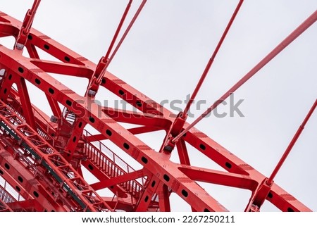 Close-up of fragment of red cable-stayed bridge pylon in place where metal cables are fastened. Close-up shows connection of steel powerful straight crossbar, bridge connection, metal architecture.