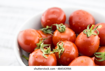 Closeup of fresh cherry tomatoes in white ceramic bowl on rustic wooden background. Ingredients for tomato sauce. Organic food. Soft focus
