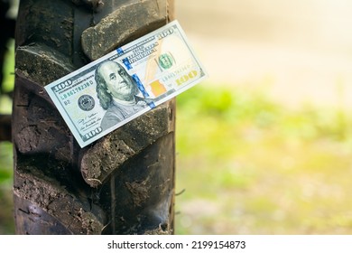 Close-up Fresh Clean Bill Of One Hundred Dollars Lies On The Tread Of A Tractor Wheel. Farmland Financing. The Cost Of Maintenance And Production On The Farm. Purchase Of Agricultural Machinery