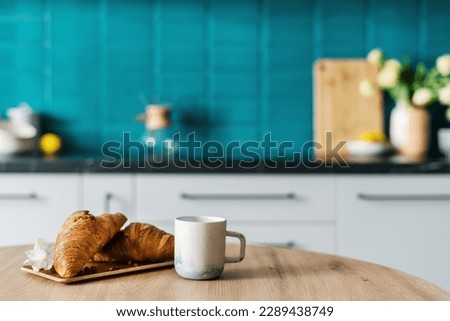 closeup of fresh croissants on bamboo plate decorated flower and cup of coffee on wooden dining table on blurred kitchen background, breakfast concept